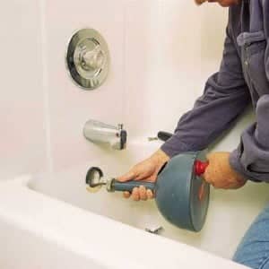 A repairman using a drain snake to clear a clogged bathtub drain