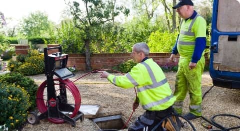 Two utility workers in reflective vests inspecting equipment next to an open manhole by a truck in a residential area.