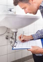 A man inspecting and taking notes on a clipboard next to a bathroom sink.