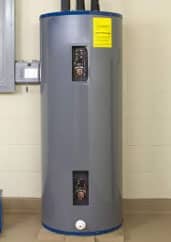 A tall, gray water heater with control panels and warning labels, installed in a room with a beige tile floor.