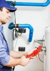 A plumber using a wrench to work on a water heater pipework.