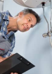 A male technician inspects an overhead fixture, holding a clipboard, with a focused expression.