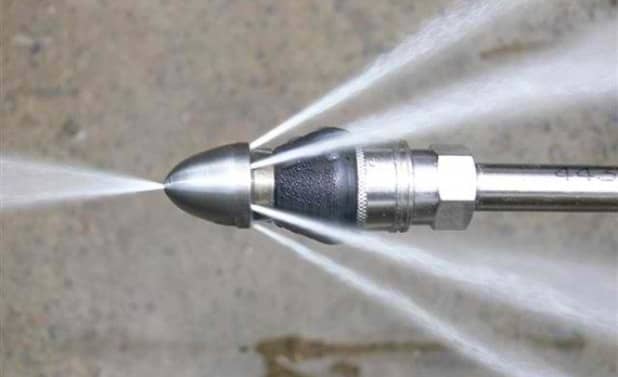 Close-up of a high-pressure spray nozzle ejecting a strong jet of water against a gray background.