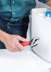 A plumber using a wrench to fix a sink in a bathroom.