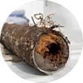 A close-up of a severely corroded and damaged metal pipe, with visible rust and a large hole, on a white background.