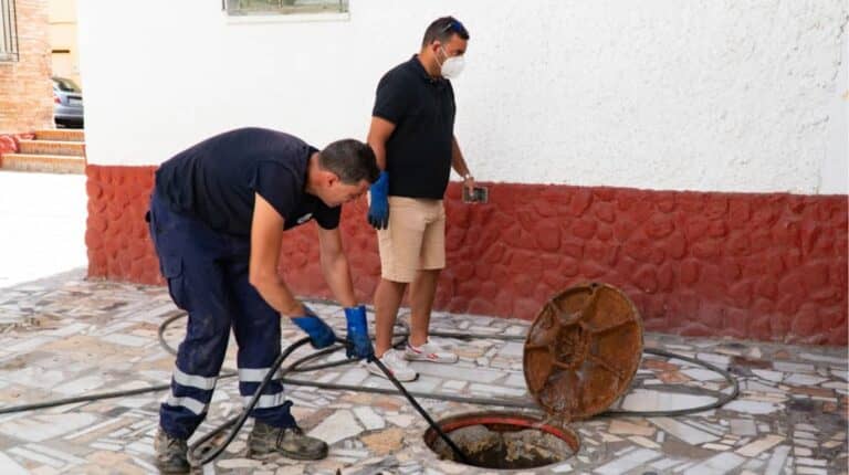 Workers cleans the drains hatch and removes dirt and debris from the sewer on the street. Repair of sewage or underground utilities, cleans drains