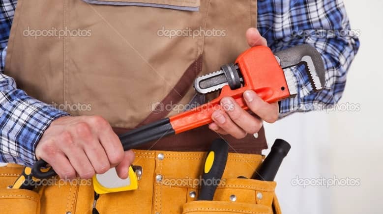 A worker in a brown apron and plaid shirt holds a red pipe wrench, with various tools in a belt around the waist.