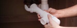 A person holding a white plumbing pipe under a sink, appearing to inspect or install it.